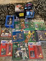 Wide view of the entire lot showing multiple Starting Lineup sports figures in blister packaging, boxed Carls Jr bobblehead, and two sealed Topps Active Flats boxes.