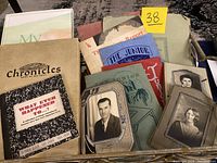 Photo showing vintage yearbooks and books including 'Chronicles From The Past' and 'What Ever Happened To?', old portrait photos, and a folder with historic documents.