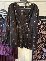 Black floral print blouse with long sleeves on hanger among dresses