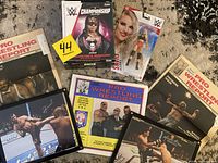 Group photo showing Bret Hart WWE Championship magazine, Lacy Evans action figure in blister packaging, three vintage Pro Wrestling Report magazines, and two framed autographed MMA fighter photos.