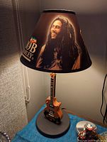 Lamp with guitar-shaped wood base and Bob Marley themed shade lit showing details and design.