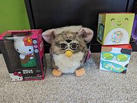 Front view of the four collectible toys: Furby, Hello Kitty Hula Dancer in box, and two McDonald's Squishmallows boxes.