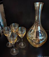 Full view of the iridescent crystal decanter with four matching stemmed glasses grouped beside it against a dark background.