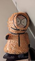 Side view of handmade South Park Kenny pinata showing details of orange fringed paper and black accents.