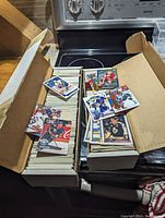 Two open cardboard boxes filled with hockey trading cards mostly from the 1990s, arranged in stacks with some cards laid on top showing players in colorful jerseys.