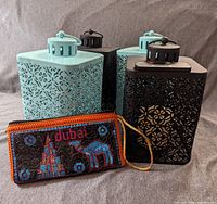Four metal lanterns and one colorful embroidered wallet arranged on a gray fabric background, showing detailed pattern and colors.