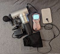 Photo showing a silver and black rechargeable muscle massager with multiple massage attachments and charging adapter. Pink TENS machine with body diagram on the screen, connected to electrode pads and a black mesh carrying pouch.