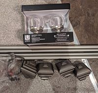 Photo showing two telescoping metal curtain rods, four attached metal finials, two glass globe finials in box, mounting hardware and plastic anchors on carpet.