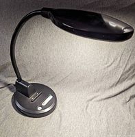 Full view of the black Powerline PowerLamp LED task light with flexible neck and elongated head, placed on a grey surface.