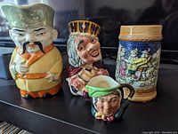 Four ceramic pieces: Old King Cole Toby Jug, Emperor Toby Jug, mini Royal Daulton Toby Jug, and unmarked stein all on shelf.