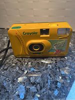 Front view of bright yellow Crayola Sport 35mm camera with lens, flash, viewfinder and control buttons visible.