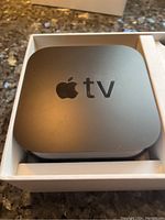 Top view of the Apple TV device in white box showing Apple logo and 'tv' text.