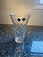 Full view of clear crystal vase standing on countertop, showing brand label and hand cut pattern on side.