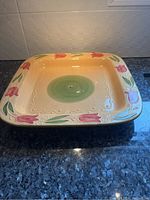 Full view of large square ceramic serving platter with colorful floral border and green center on a dark surface.
