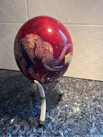 Side view of ceramic decorative egg with detailed elephant design and stand with three curved legs.
