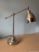 Full view of the desk lamp showcasing the base, upright stem and the adjustable arm with dome-shaped shade in polished stainless steel.