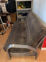 Side view of futon showing silver metal frame, armrest, and leopard print mattress and backrest.