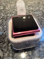 Front view of pink Apple iPod Nano inside plastic casing placed on a reflective surface.