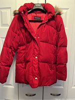 Red puffy winter jacket hanging on hanger showing front, hood has removable faux fur trim.