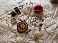 Overview of assorted costume jewelry and accessories laid out on white sheet, showing variety of necklaces, bracelets, earrings, and small purses.