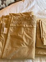 Queen size beige linens set with detailed embroidery showing folded fitted sheet, flat sheet, and pillow cases