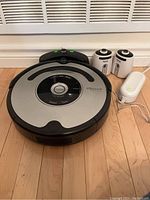 Photo showing iRobot Roomba robotic vacuum cleaner along with the charging station and two virtual wall units on a wooden floor.
