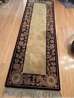 Full view of the thick plush runner carpet with beige center and floral border on black field, fringed edge visible.