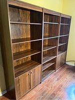 Three wooden shelving units placed side by side showing overall condition and design, including adjustable shelves and two-door bottom cabinets on two units