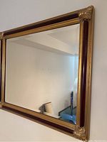 Full view of rectangular mirror with gold and wood tone frame and decorative corners.