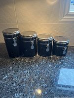 Four sizes of black ceramic canisters with metal clamp lids in closed position on a kitchen counter