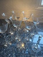 Eight clear glass wine goblets displayed on a dark granite countertop, showing twisted stems and wide bowls.