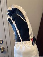 Side view of one Spider women's white winter snow glove showing black palm area, padded white back, elastic wrist, and a clip.