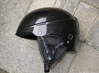 Side view of glossy black child ski helmet showing shape and attached chin strap.