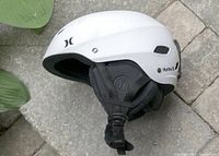 Side view of white Hurley ski helmet showing vents, logo and ear pads with adjustable strap.