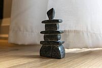 Full side view of the dark soapstone Inukshuk sculpture showing its stacked flat stone shapes and pointed top stone.