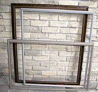 Three large wood frames leaning against a brick wall, showing varying finishes and sizes.