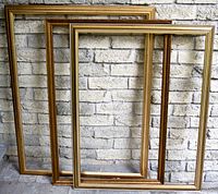 Three large gold-toned picture frames leaning against a brick wall, showing sizes and relative shapes.