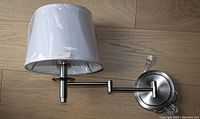 Wall lamp shown fully extended with protective cover on fabric shade, resting on wooden surface.
