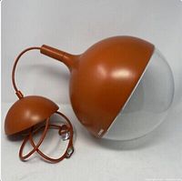 Orange Ikea Väster pendant lamp laid on side showing full lamp and metal canopy with cord and plug, on white background.