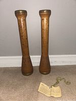 Pair of tall wooden candleholders made from restored wool spinning bobbins, standing against a wall on carpet.