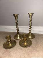 Photo showing all four brass candlesticks together, two taller twisted stem candlesticks and two smaller round base candlesticks.