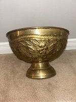 Side view of the brass fruit bowl showing embossed grape and leaf pattern and pedestal base.