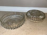 Two clear round crystal bowls showing sides and tops, featuring diamond facets and starburst base patterns, placed on carpet in front of white baseboard.