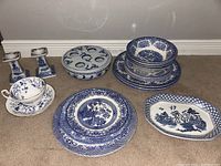 Wide angle of the lot showing all items on the floor including plates, bowls, candlesticks, cup and saucer, and egg holder bowl.