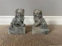 Front view of pair of marble Foo Dog bookends on floor against white baseboard.