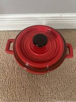 Top view of a small red mini cocotte baking dish with lid, showing black knob and embossed 'MINI COCOTTE' lettering on lid top.