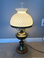 Full view of vintage brass lamp with milk glass hobnail shade illuminated, showing base and textured shade with ruffle edge.