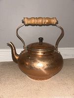 Front view showing rounded brass kettle body, spout, hinged lid with knob, and curved brass handle with wooden grip.