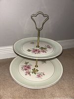 Full view of the two-tier cake stand showing the floral pattern and gold handle.