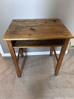 Front view of vintage wooden child’s school desk showing the desktop, four angled legs, and storage compartment underneath.